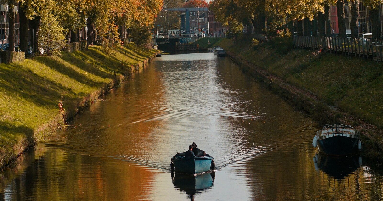 A small boat cruising down a calm canal lined with golden autumn foliage reflected in the still water