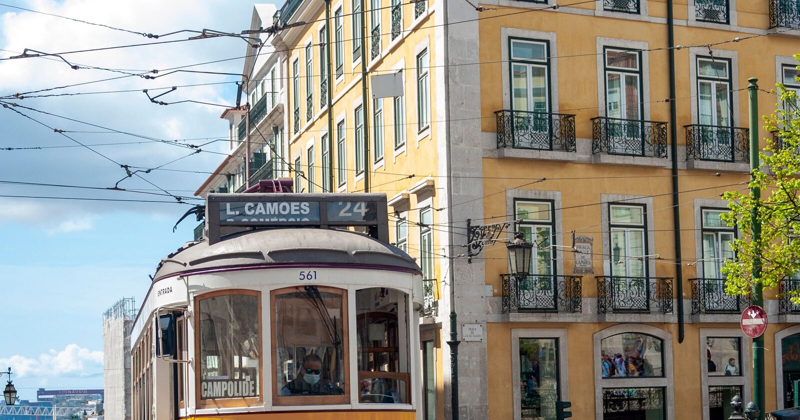 A vintage yellow Lisbon tram passing tiled, pastel buildings under a blue sky in the old town